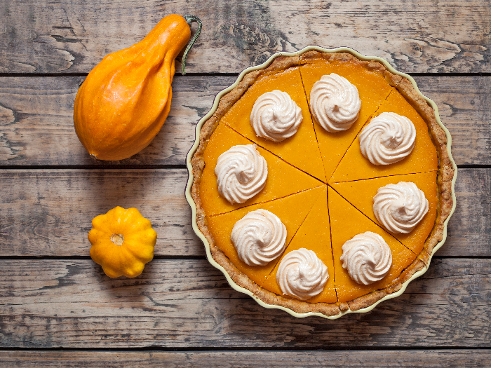 Two small pumpkins besides a whipped cream topped pumpkin pie
