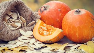Close-up of two pumpkins, one-quarter pumpkin and a burlap sack full of pumpkin seeds.