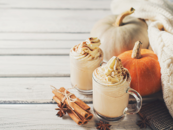 Two cups of pumpkin spice latte with cinnamon and star anise and pumpkins kept beside them atop a white table