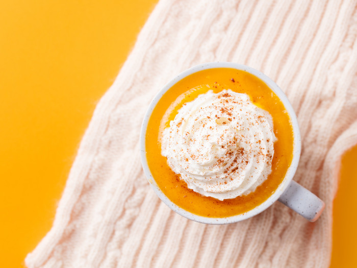 A flat-lay image of a cup of pumpkin spice latte with whipped cream kept atop a white towel on a yellow table