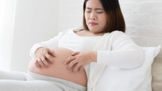 Pregnant woman with exposed belly looking uncomfortable