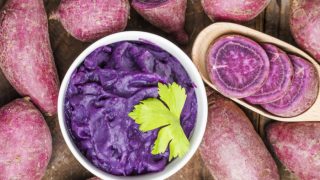 Purple potatoes spread on a table and a bowl of potato mash kept in th middle