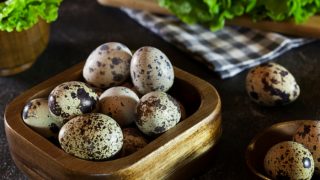 A wooden basket and bowl of quail eggs with leaves on a dark background