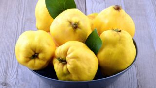 A bunch quince fruits in a round green bowl on a wooden table