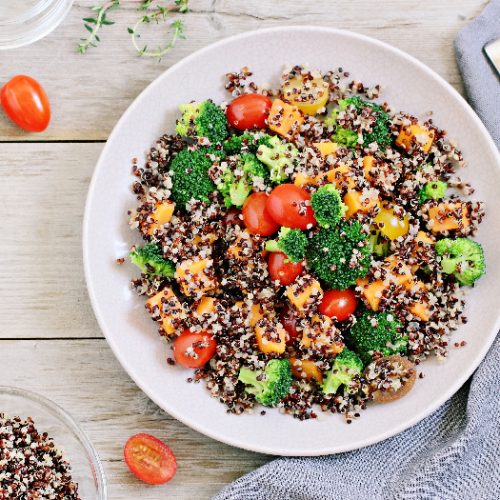Quinoa salad with broccoli, sweet potatoes and tomatoes on a rustic wooden table. Three-color quinoa salad
