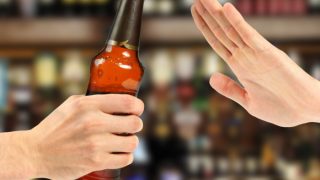 Close up of a hand of a person offering alcohol bottle and another person's hand denying the offer