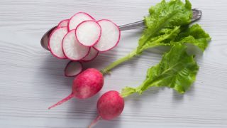 Fresh pink whole and sliced radish with leaves on a white marble