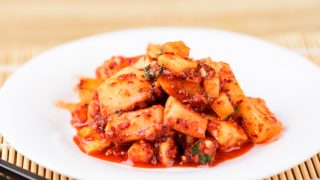 A close up shot of radish kimchi kept on a white plate with chopsticks