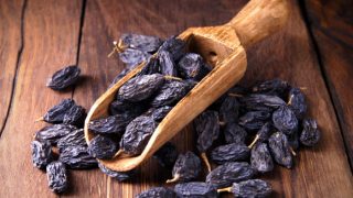 Black raisins in a rustic spoon on wood