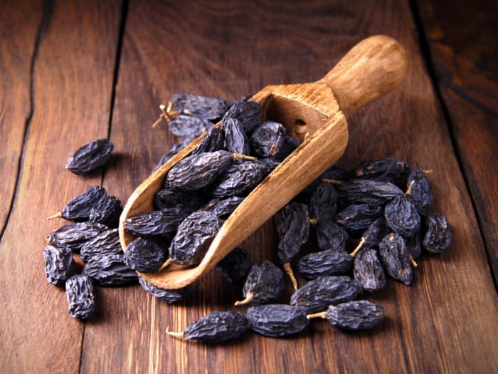 a wooden spoon full of black raisins kept on a table