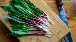 Fresh wild ramps on a wood cutting board next to a knife