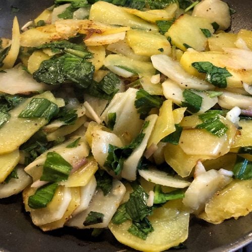 Fried potatoes and ramps on a black plate