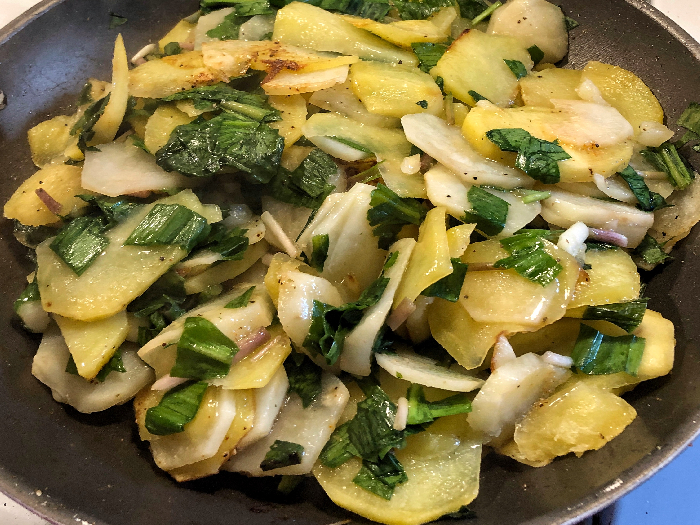 Fried potatoes and ramps on a black plate