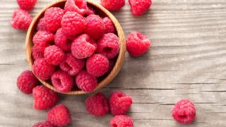 A wooden bowl filled with fresh raspberries kept on a wooden table