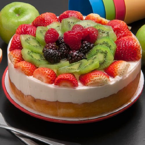 Paleo Vanilla cheesecake garnished with fresh fruits like strawberries, kiwis, and blue berries, kept atop a plate on a table