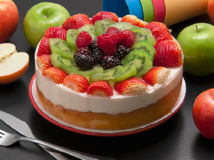 Paleo Vanilla cheesecake garnished with fresh fruits like strawberries, kiwis, and blue berries, kept atop a plate on a table