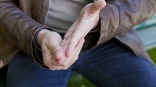 A man sitting on a bench suffering from cold fingers which is a symptom of Raynaud's disease