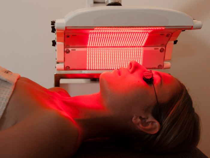 Woman lying on a bed receiving red light therapy on her face