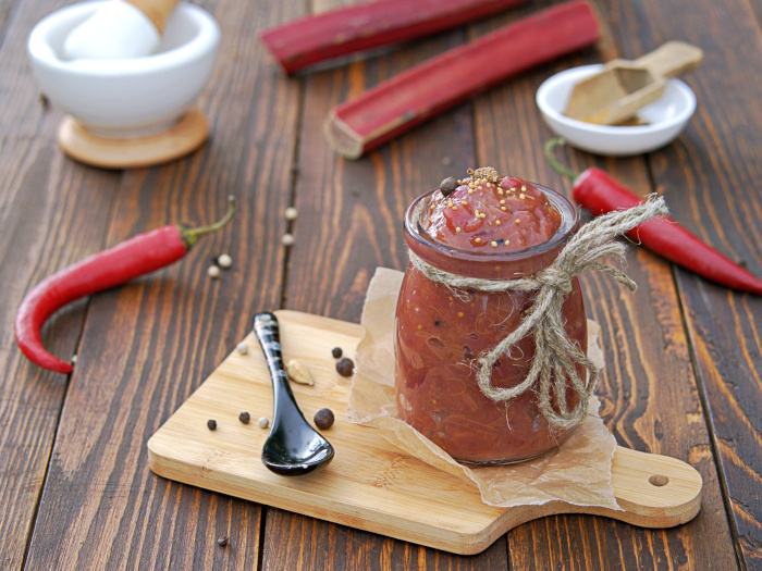 Spicy rhubarb chutney sauce in a glass jar on a wooden background