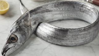 Raw ribbonfish on a marble counter, with sliced lime and a knife in the background