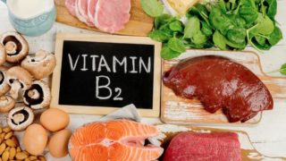 Foods rich in vitamin B2 or riboflavin (Slices of beef, pork, and fish, mushrooms, almonds, eggs, sliced cheese, spinach, and a mug of milk) on a wooden table