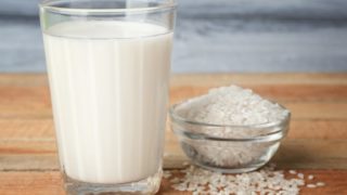 Bowl of rice and a glass of milk on a wooden surface.