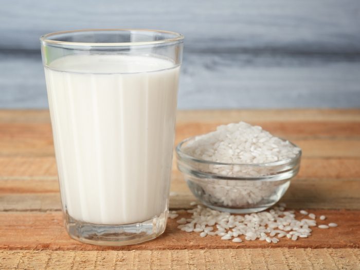 Bowl of rice and a glass of milk on a wooden surface.