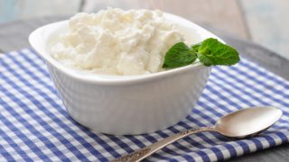 A bowl of ricotta cheese placed on a blue-checked cloth with a spoon.