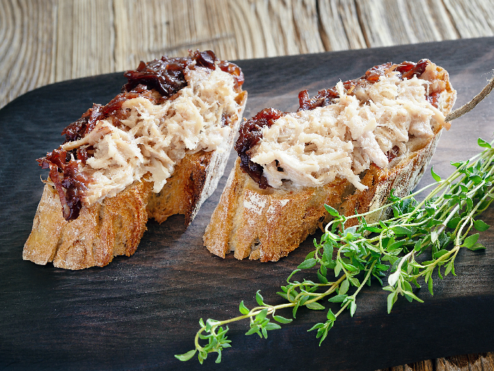 Meat rillettes on bread and a glass jar with the jam covering rillettes