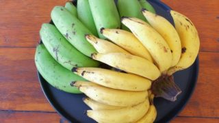 Yellow ripe bananas and green raw bananas on a black dish on wood