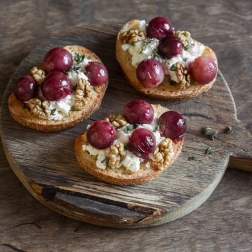 Roasted grape and goat cheese bruschetta on a wooden background.