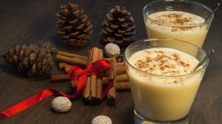 Rompope in a glass with a spoon next to cinnamon sticks on a wooden surface
