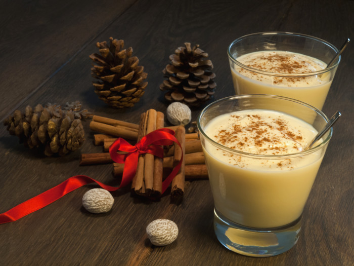 Rompope in a glass with a spoon next to cinnamon sticks on a wooden surface