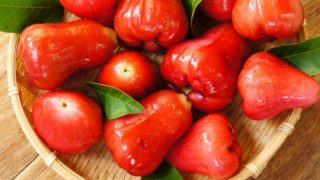 A basket of fresh ripe rose apples with leaves on a wooden table