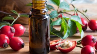 Rosehip essential oil bottle, next to rosehip berries, split rosehip berries with seeds, and leaves