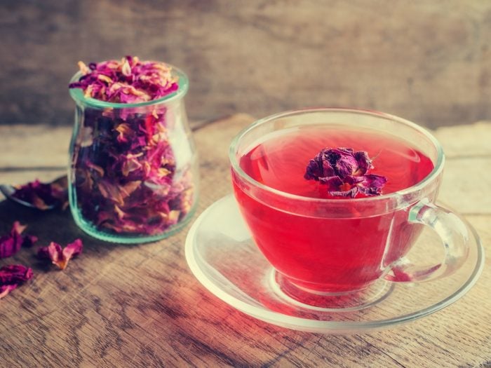 A jar filled with dried rose leaves and a cup of rose tea on a wooden table