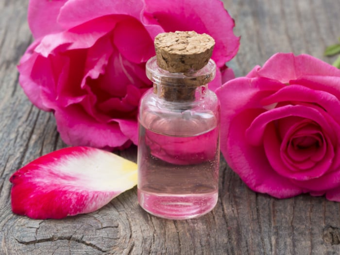 Bottle of rosewater and rose flowers at the back on a wooden surface.