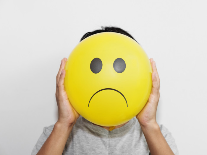 A person holding a balloon with a sad emoji