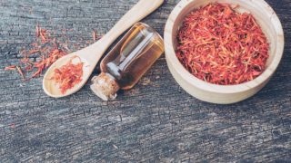 Safflower oil in a bottle, dried safflower in a wooden bowl and spoon
