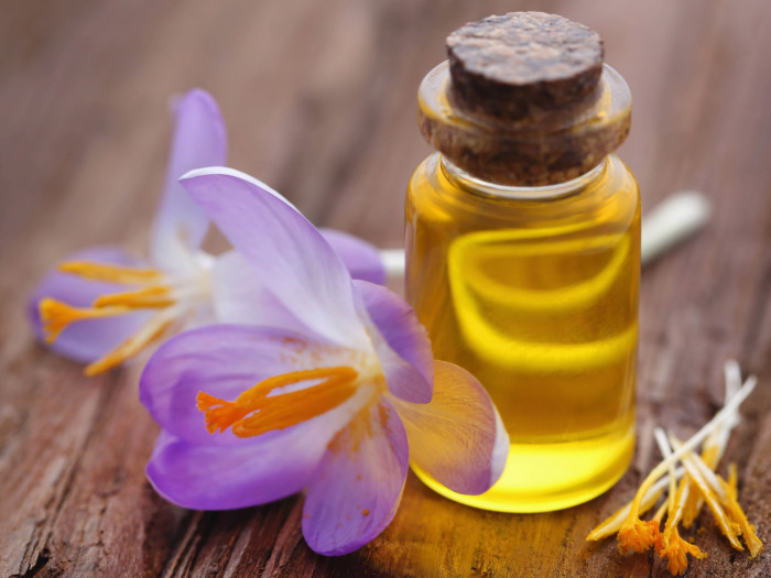 A container of saffron oil with fresh saffron flowers on a wooden table