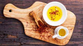 Saffron herb in a spoon, next to saffron oil and saffron tea on a wooden board
