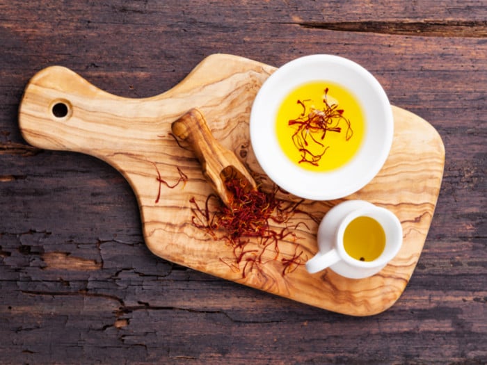 Saffron herb in a spoon, next to saffron oil and saffron tea on a wooden board