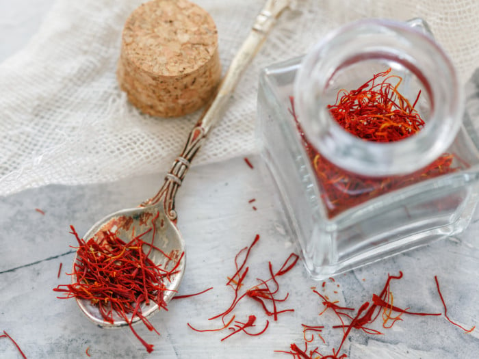 An open jar of saffron and a spoon filled with saffron on a table