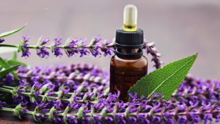 A small dropper bottle of sage oil with fresh sage flowers and leaves on a wooden table