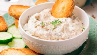 Smoked salmon spread in a bowl with a bruschetta and a plate of bruschetta and cucumber slices