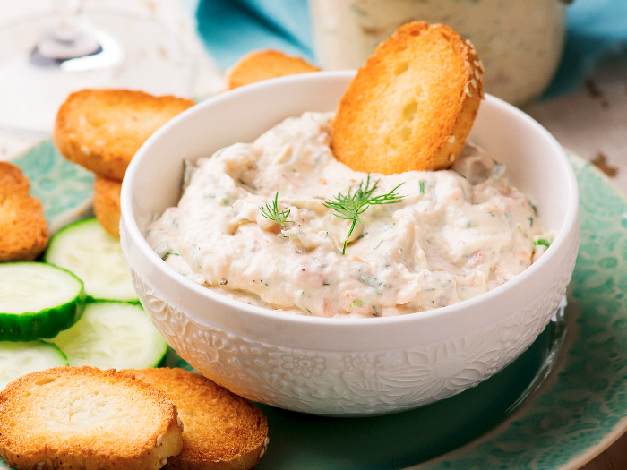 Smoked salmon spread in a bowl with a bruschetta and a plate of bruschetta and cucumber slices