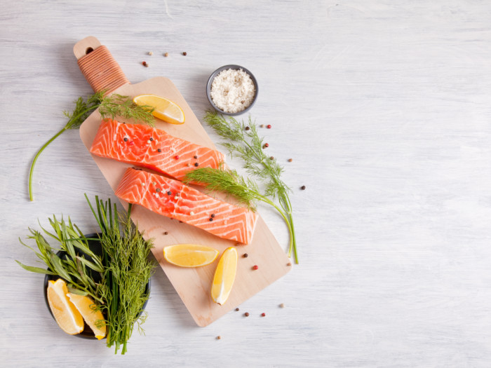 Raw salmon on a wooden board with lemon slices, dill, sea salt, and peppercorns