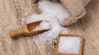 A sack of sea salt spilled on the table, a wooden scoop, and plate of sea salt on a wooden table
