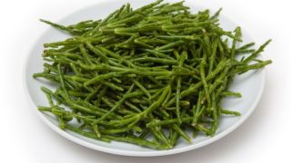 A white plate filled with fresh samphire on a white background