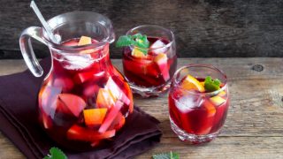 A pitcher and two glasses of red wine sangria with sliced fruits and mint